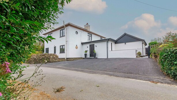 A two-story house with a paved driveway, a stone wall, and a black gate. - Bag-end House 7 Bedrooms, Sleeps 14, Hot Tub (Braunton)