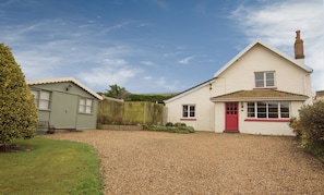 A two-story house with a red door and a small shed to the left.
