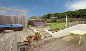 A wooden deck with a hot tub, a purple bench, and a yellow table.