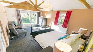 Quarto com cama, sofá, escrivaninha, luminária e janela com cortinas.