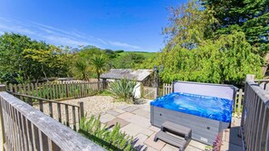 A hot tub in a backyard with a wooden fence, stone pathway, and lush greenery. - Streamways Nr Croyde 6 Bedroom, Sleeps 12-16, Hot Tub  (Braunton)
