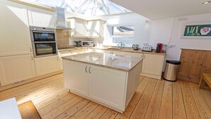 A modern kitchen with white cabinetry, a central island, a skylight, and wooden flooring. - Stables Croyde 4 Bedrooms, Sleeps 8, Sea & Beach Views (Braunton)