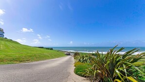 A coastal road with a grassy hill, a building on the left, and the ocean in the distance. - Stables Croyde 4 Bedrooms, Sleeps 8, Sea & Beach Views (Braunton)