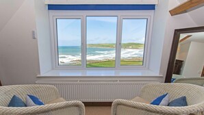 A room with a large window overlooking the sea, two wicker chairs with cushions, and a white radiator below the window. - Stables Croyde 4 Bedrooms, Sleeps 8, Sea & Beach Views (Braunton)