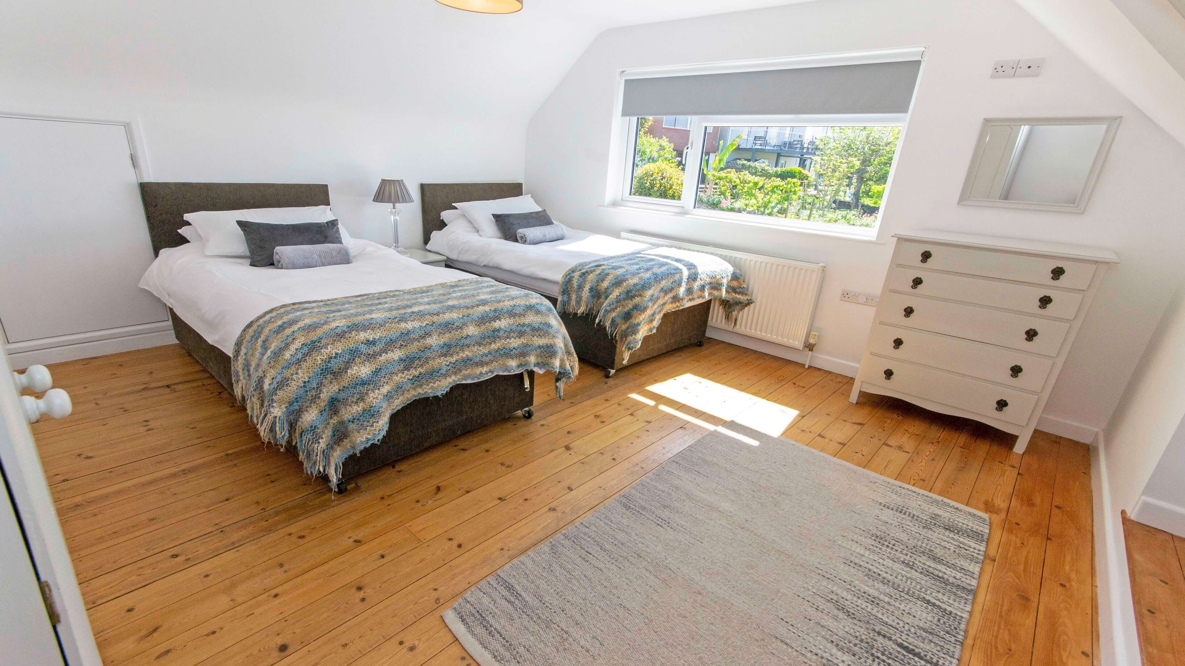 A bedroom with two beds, a dresser, a radiator, and a window with a view.