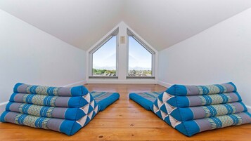 Una habitación con techo inclinado, suelo de madera y dos ventanas amplias con vistas a la ciudad.