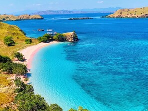 A coastal landscape with clear turquoise waters, a sandy beach, and boats in the distance. - World BnB (Labuan Bajo)