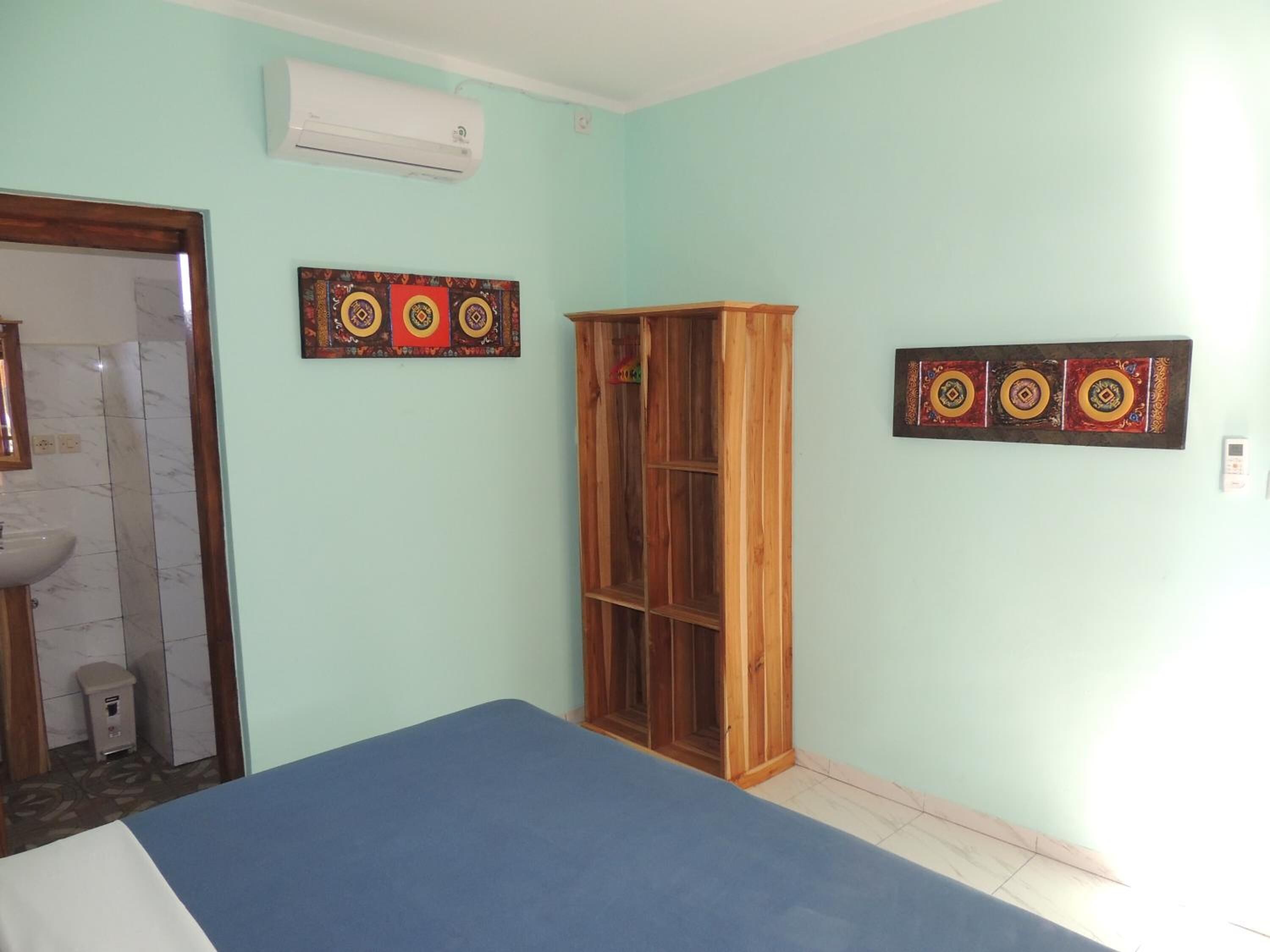 A room with a bed, a wooden wardrobe, a wall-mounted air conditioner, and two decorative wall panels.