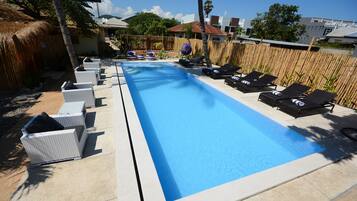Una piscina rectangular con sillas de descanso y una valla de bambú al fondo.