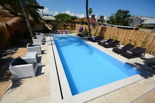Una piscina rectangular con sillas de descanso y una valla de bambú al fondo.
