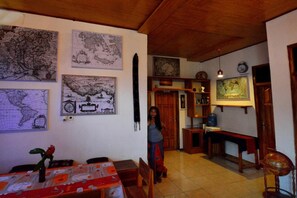 A dining area with a table set for two, a wooden ceiling, and a bookshelf with various items. - World BnB (Labuan Bajo)
