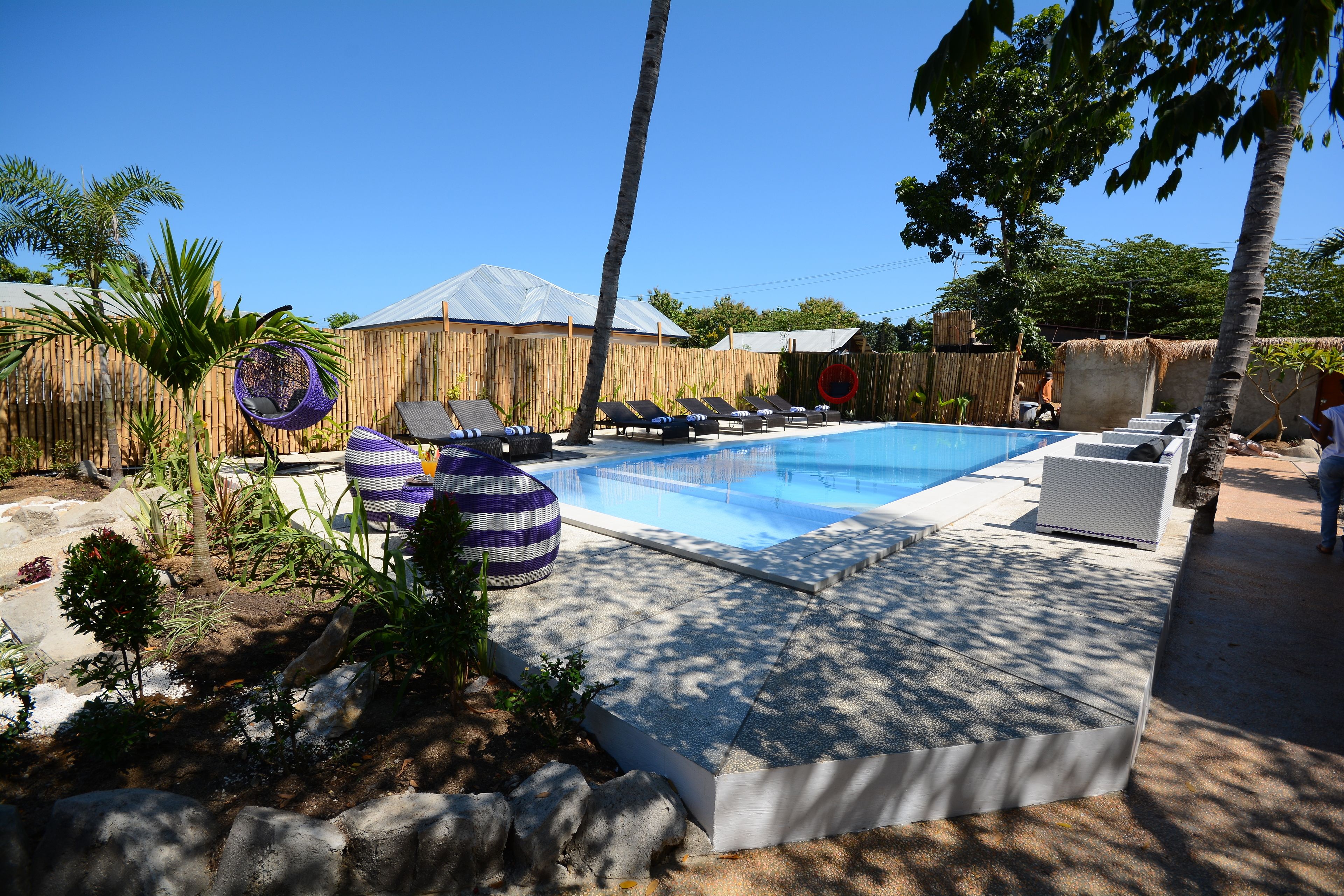 Une piscine avec des chaises longues et une clôture en bambou.