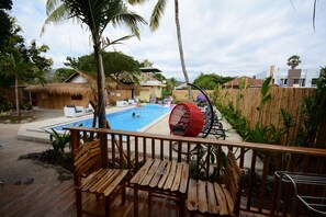 A wooden deck with a pool, lounge chairs, and a red hanging chair. - World BnB (Labuan Bajo)