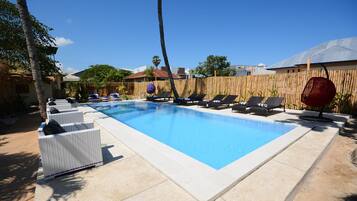 A rectangular swimming pool with lounge chairs and a bamboo fence in the background.