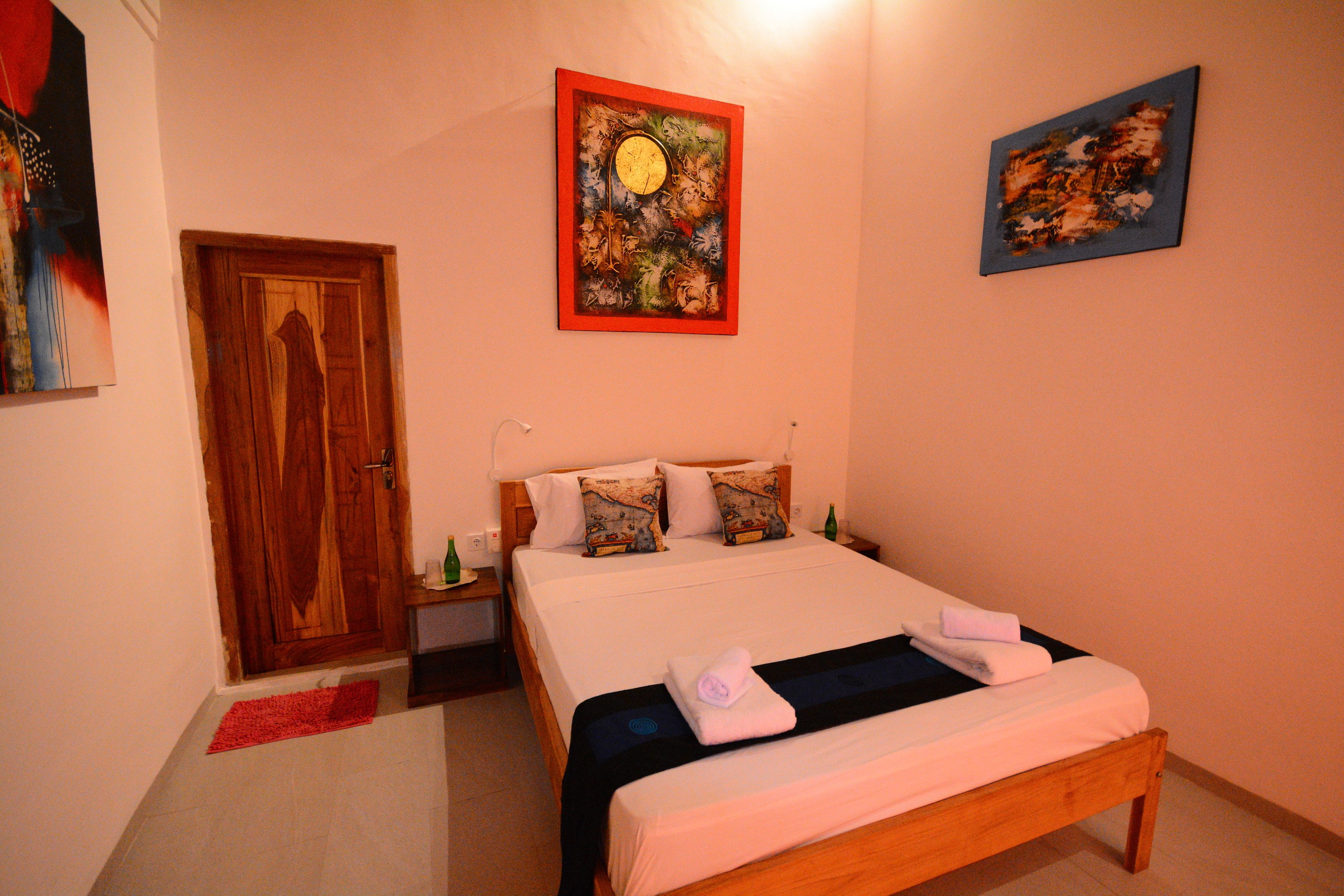 Une chambre d’hôtel avec un lit en bois, une porte rouge et deux tableaux accrochés aux murs.