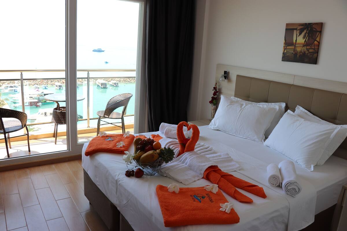 A hotel room with a bed, a window with a view of a pool and boats, and a painting on the wall.