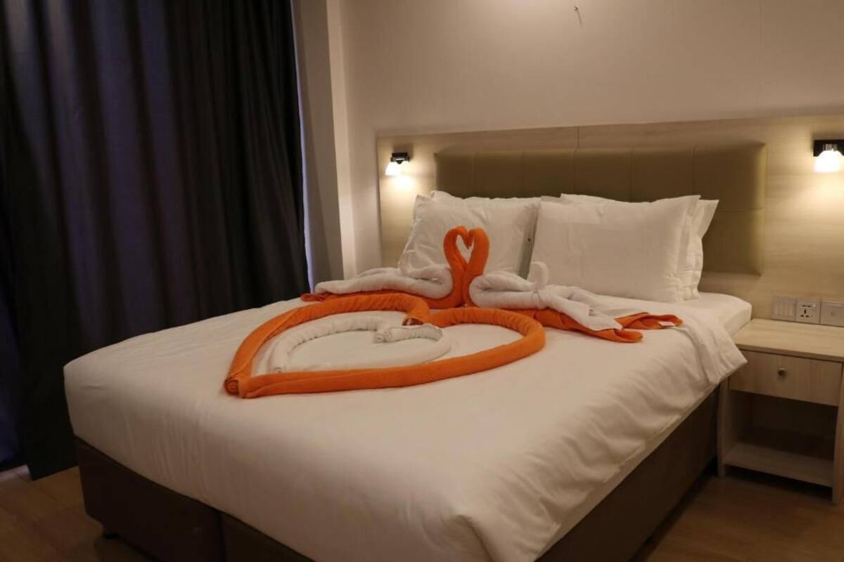 A hotel room with a neatly made bed, a bedside table with a lamp, and a window with curtains.
