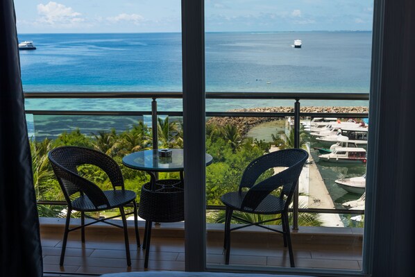 A balcony with two wicker chairs and a small table, overlooking a marina with boats and a clear view of the ocean.