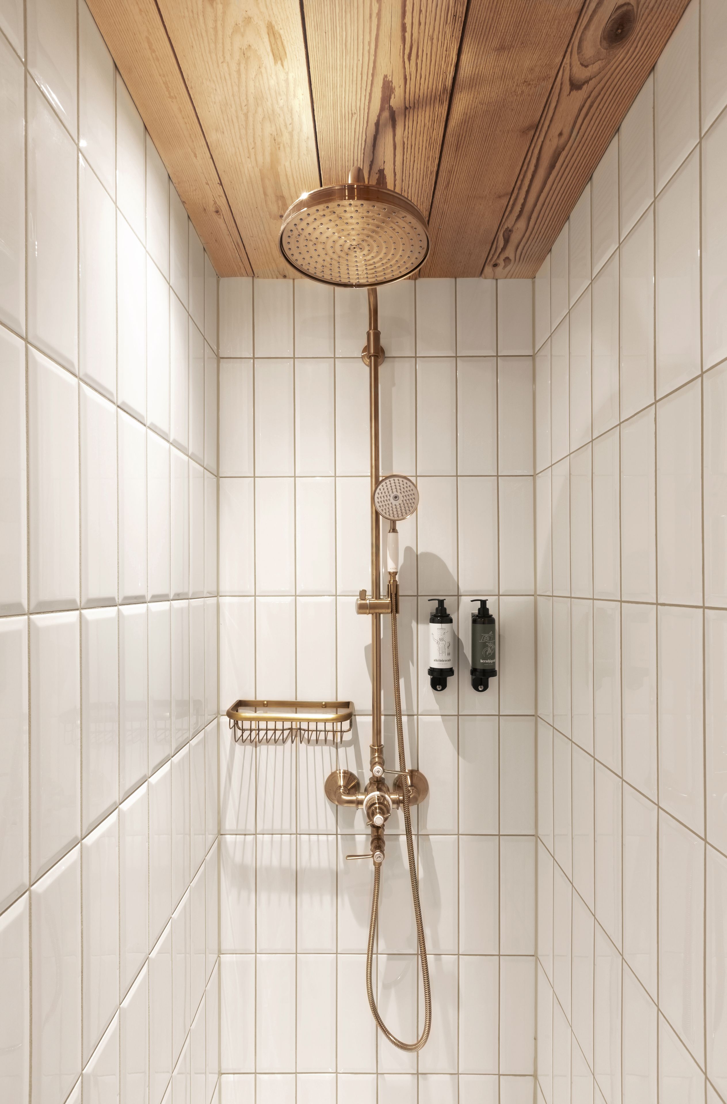 Une douche avec un plafond en bois, des murs recouverts de carreaux blancs et une pomme de douche à main.