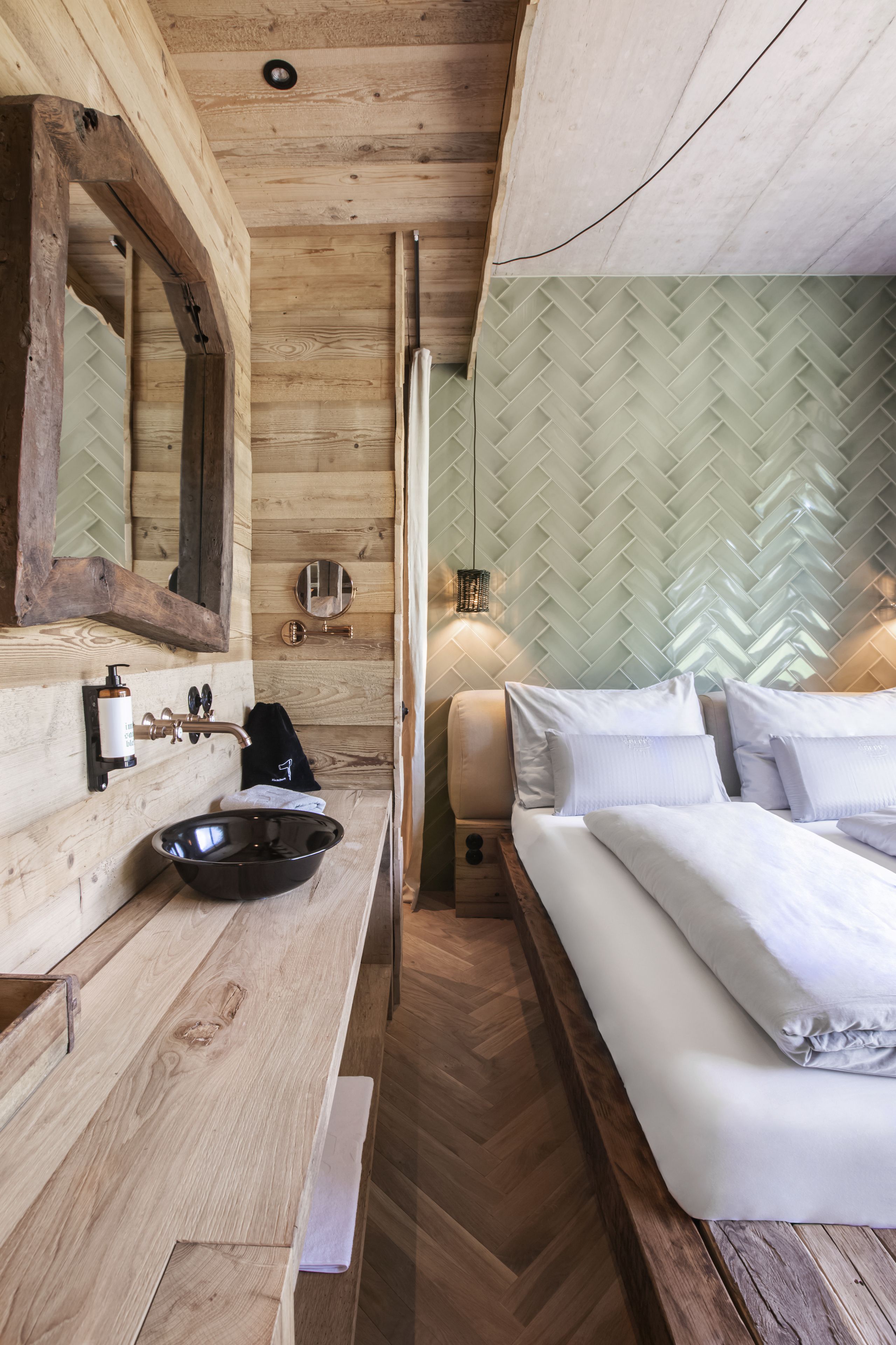 A wooden cabin interior with a wooden floor, a sink, a mirror, a bed, and a wall with a herringbone pattern.