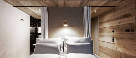 Ein Schlafzimmer mit Holzboden, einem Bett mit weißer Bettwäsche und einem kleinen Regal mit Handtüchern.