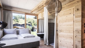 A modern bedroom with a large bed, a view of the outside, and a wooden wall. - SEPP - Alpine Boutique Hotel (Maria Alm am Steinernen Meer)