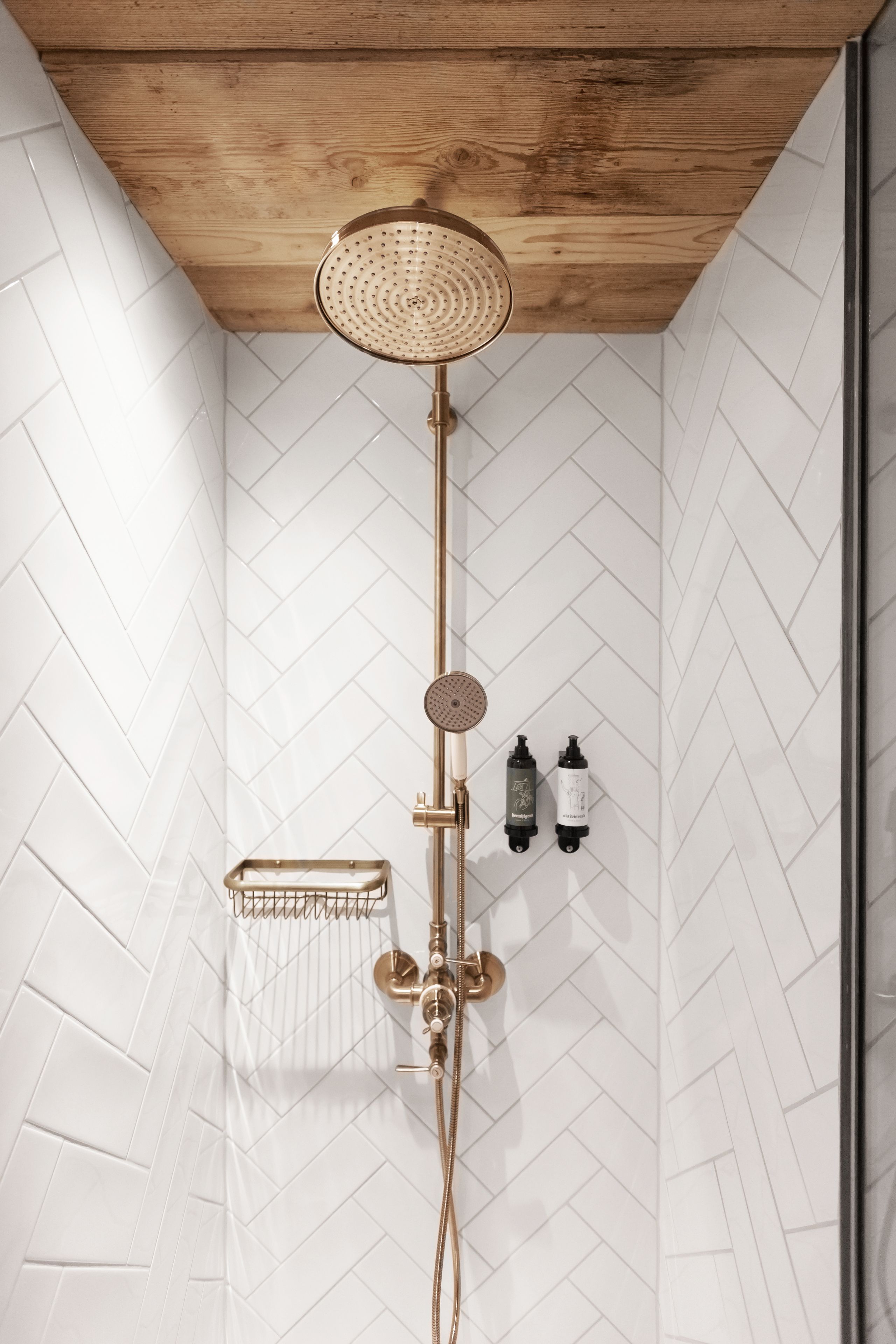 A shower with a wooden ceiling, white herringbone-patterned walls, and a gold showerhead.