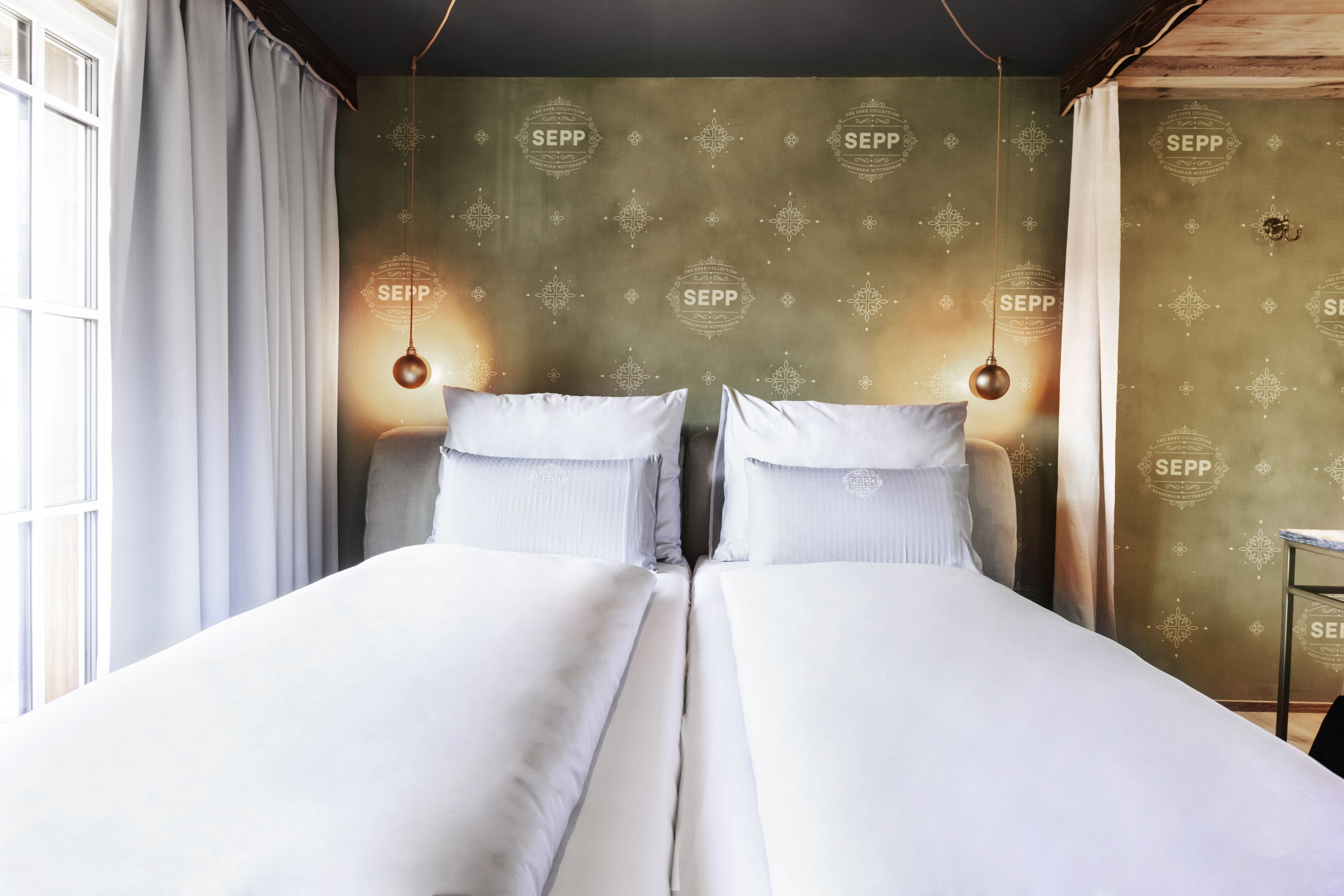 Una cama doble con ropa blanca, una ventana con cortinas, y una pared con un estampado repetido y el texto "SEPP".