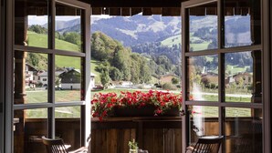 A room with a large window overlooking a scenic valley, wooden furniture, and a small table with a drink. - SEPP - Alpine Boutique Hotel (Maria Alm am Steinernen Meer)