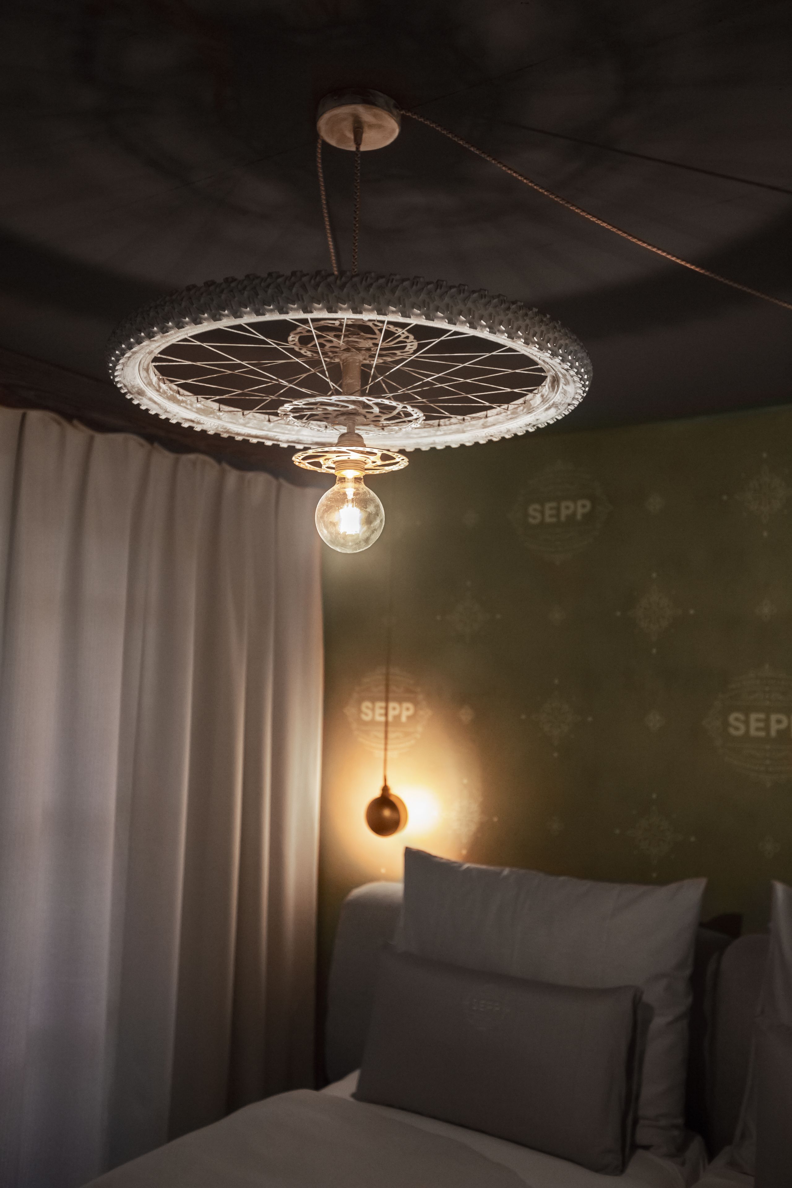 Une pièce avec un lit, un luminaire suspendu et un mur orné d’un motif répété.