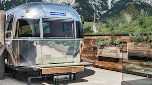 A vintage camper parked on a patio with wicker furniture and a view of mountains. - SEPP - Alpine Boutique Hotel (Maria Alm am Steinernen Meer)