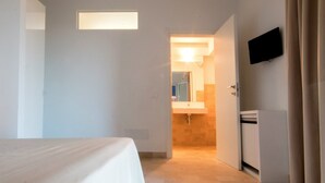 A hotel room with a bed, a TV mounted on the wall, and a bathroom visible through an open door. - Melus Maris (Syracuse)