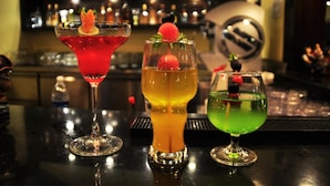 Three cocktails on a bar counter with a blurred background of shelves and bottles. - Kyriad Hotel Indore (Indore)
