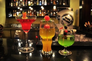 Three cocktails on a bar counter with a blurred background of shelves and bottles. - Kyriad Hotel Indore (Indore)