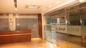 A reception area with a wooden desk, a glass wall with signage, and a ceiling with recessed lighting. - Kyriad Hotel Indore (Indore)