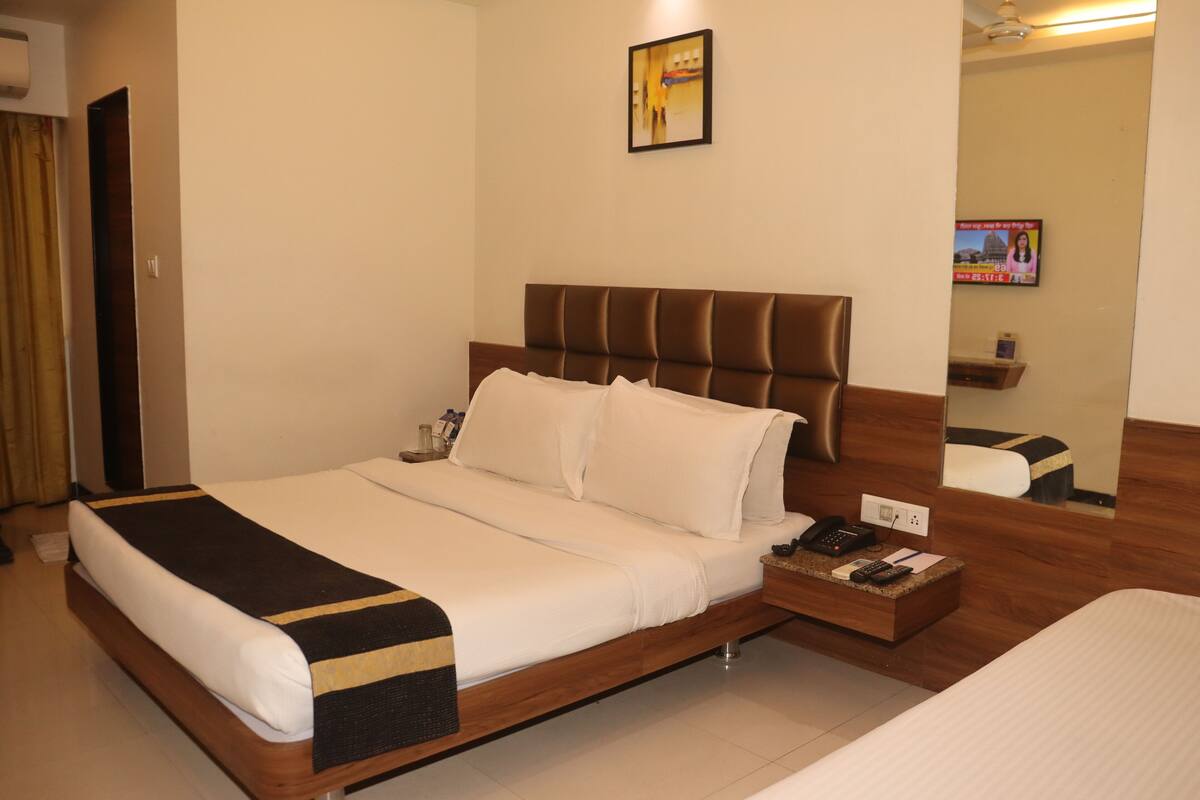 A hotel room with a large bed, a bedside table with a phone and remote, and a mirror on the wall.