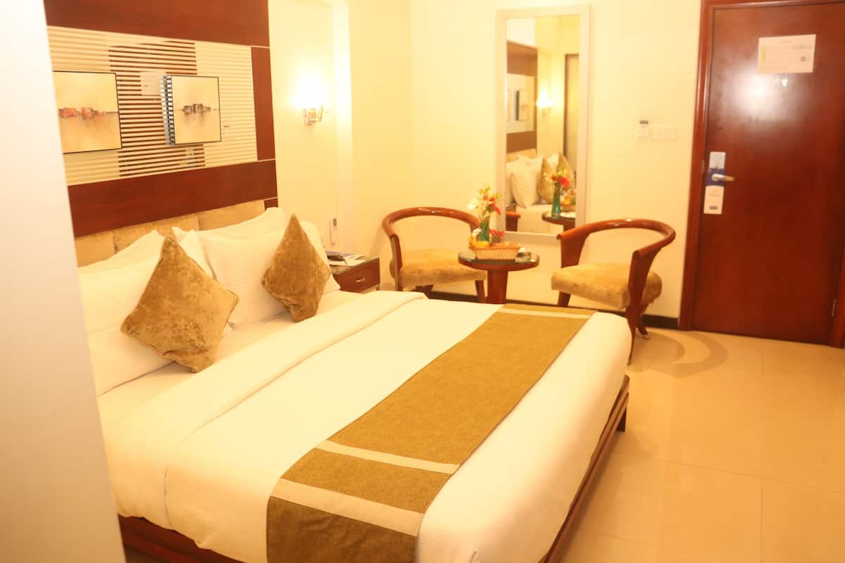 A hotel room with a large bed, two chairs, a small table, and a mirror.