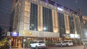 A building with multiple signs including 'Bisco Roof Top Restaurant' and 'PUNCHIN'. There are parked cars and potted plants in front. - Kyriad Hotel Indore (Indore)