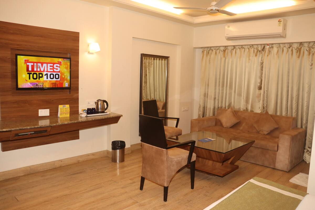 A living room with a glass coffee table, a sofa, a TV mounted on a wooden wall, and a ceiling fan.