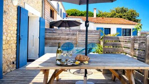 Um deck de madeira com uma mesa posta para refeição, uma garrafa de vinho e uma cesta de pão.