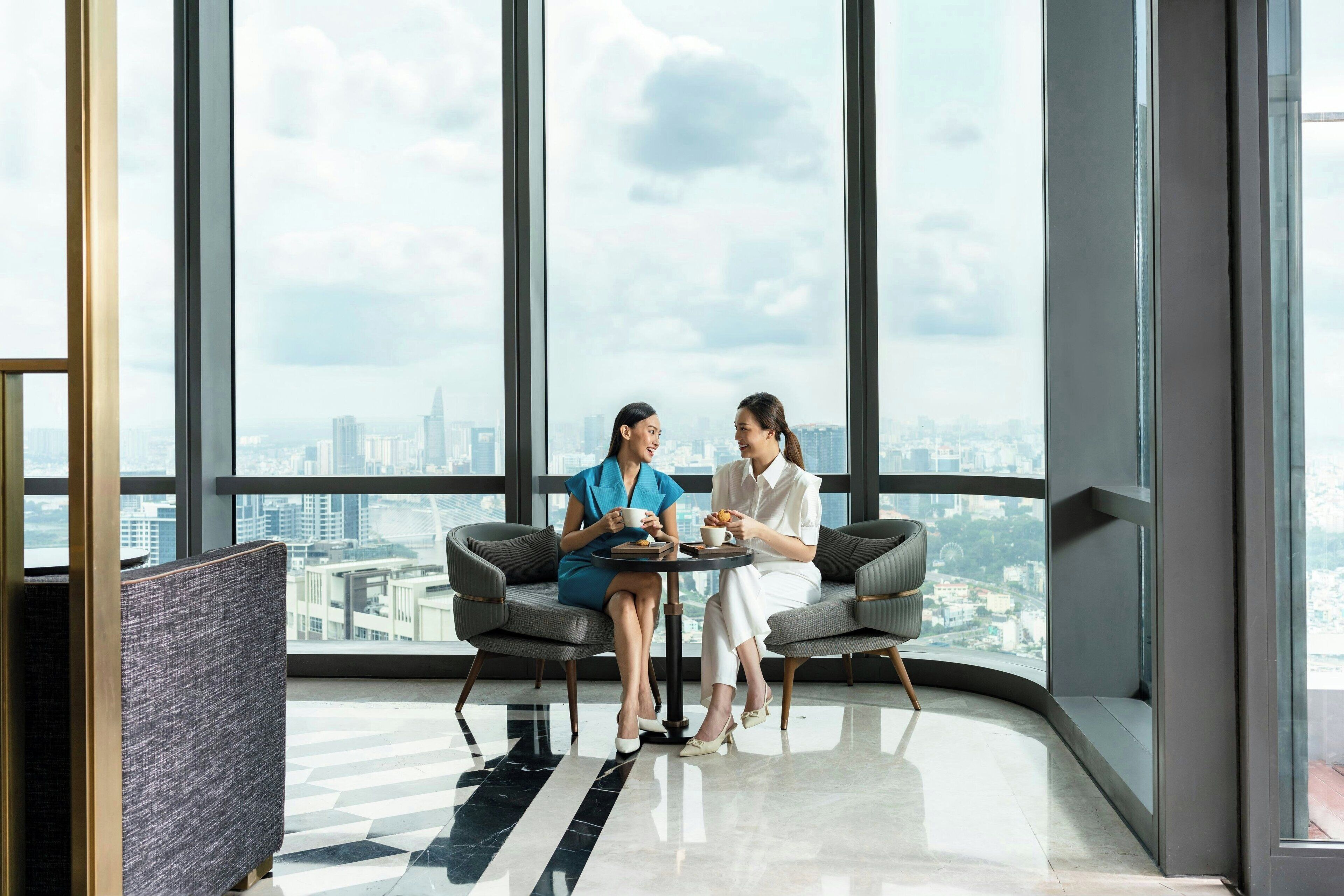Two people sitting at a table in a modern room with large windows offering a city view.