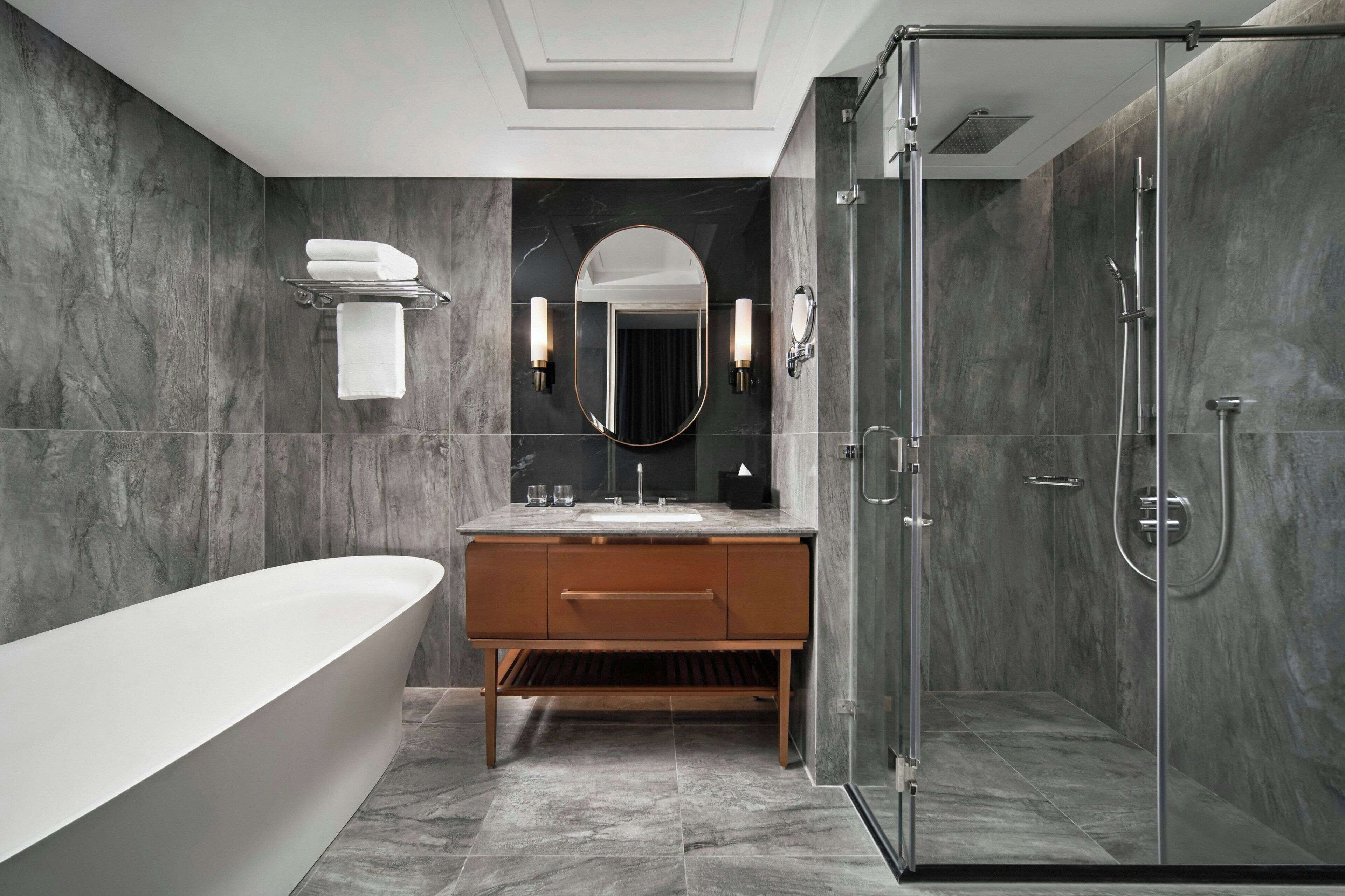 Un baño moderno con una bañera independiente, un tocador con espejo y apliques, y una ducha a pie.
