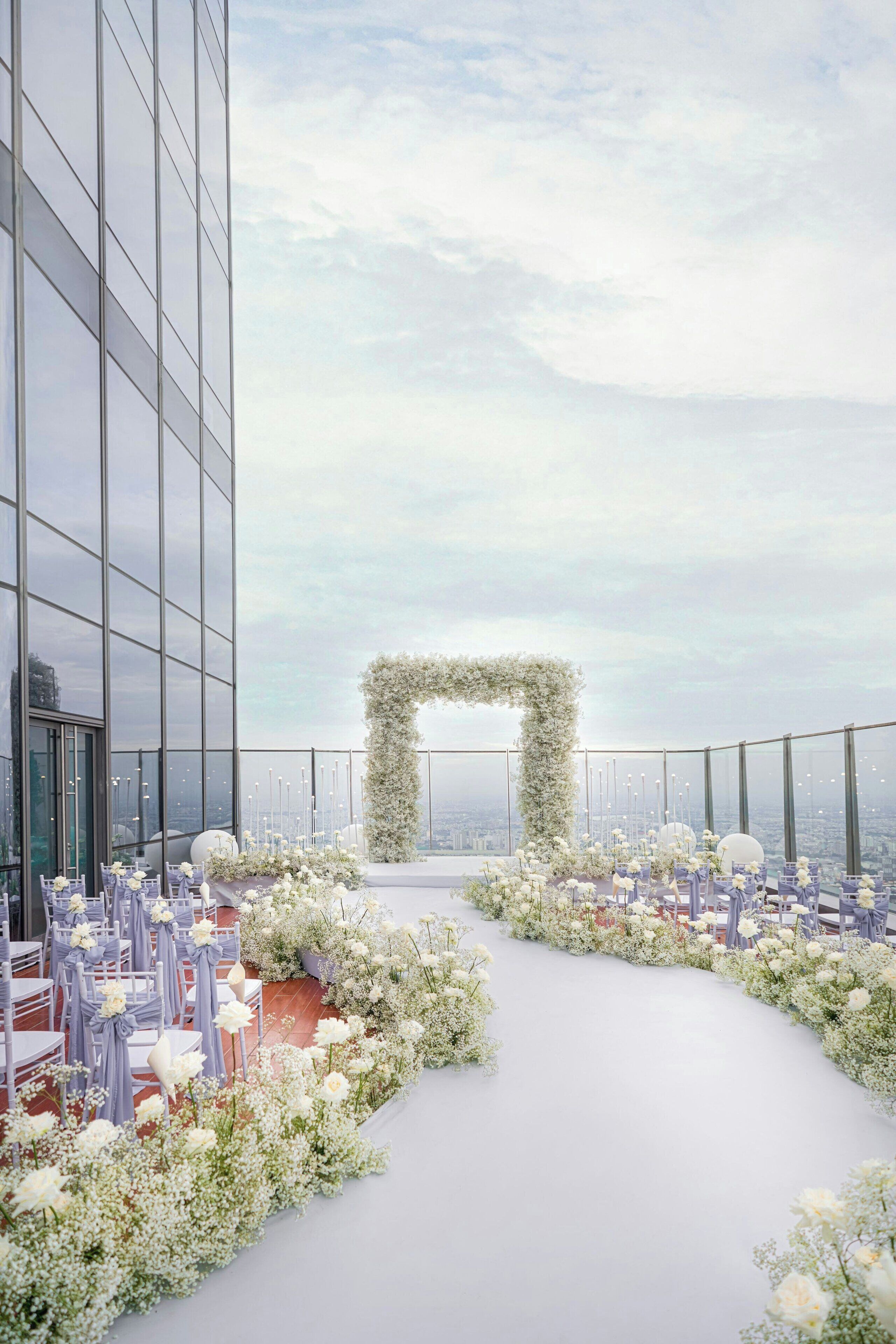 En tagterrasse med blomsterpyndet buegang, borde og stole sat frem til et arrangement.