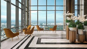 Un vestíbulo amplio con ventanas grandes que ofrecen vistas a la ciudad, asientos modernos y plantas decorativas.