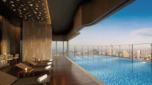 Una piscina infinita en la azotea con vistas a la ciudad, terraza de madera y sillones de descanso.