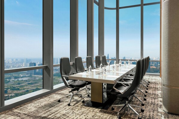 Une salle de conférence avec une longue table, des chaises noires et une vue sur la ville grâce à de grandes fenêtres.