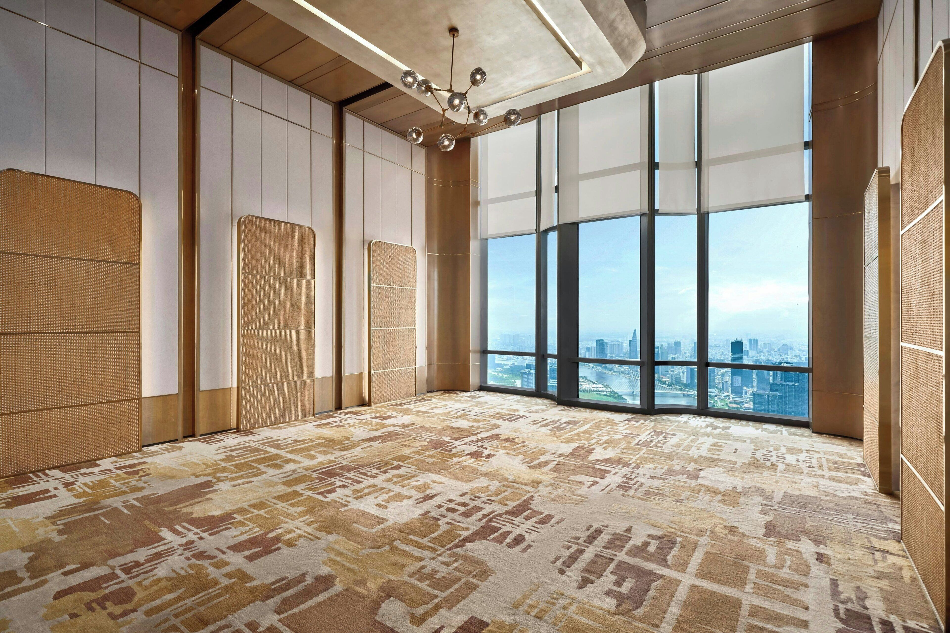 Ein geräumiges Zimmer mit großen Fenstern und Blick auf die Stadt, einem gemusterten Teppich und einer modernen Kronleuchter.