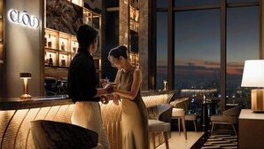 Un moderno vestíbulo de hotel con zona de bar, amplias ventanas con vistas a la ciudad y un rincón de descanso acogedor.