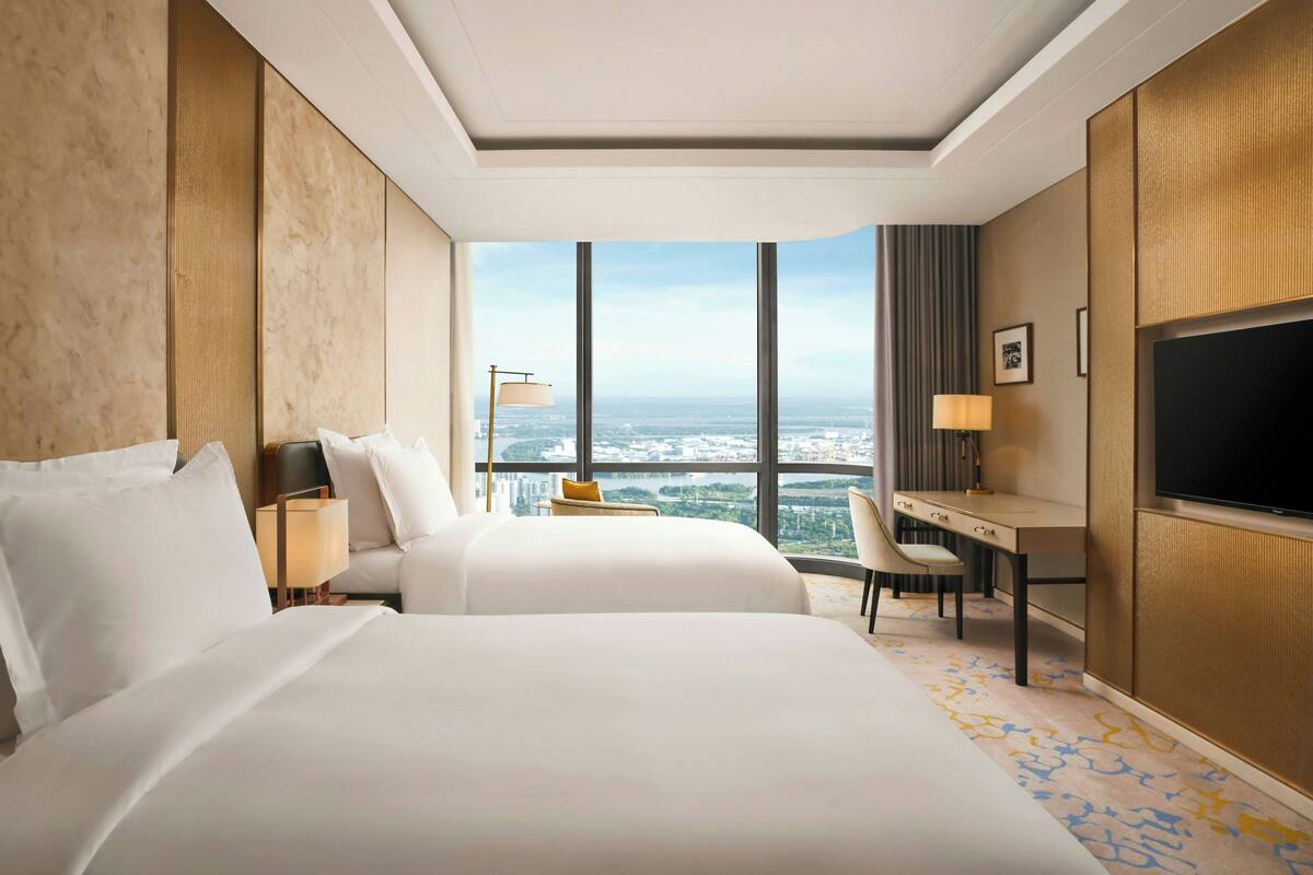 Habitación de hotel con dos camas, un escritorio, televisión y vistas a la ciudad.