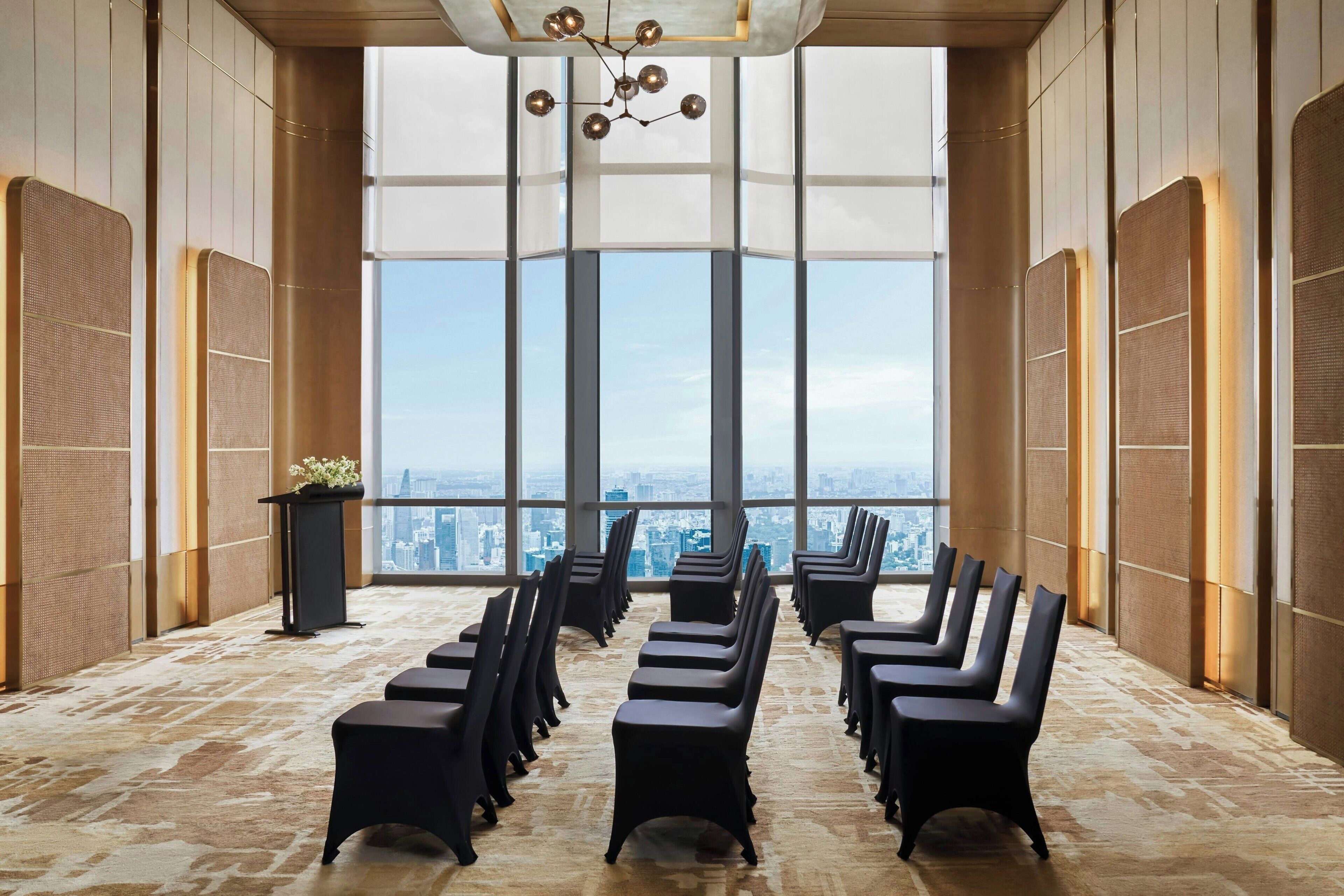A conference room with rows of chairs facing a large window with a city view.
